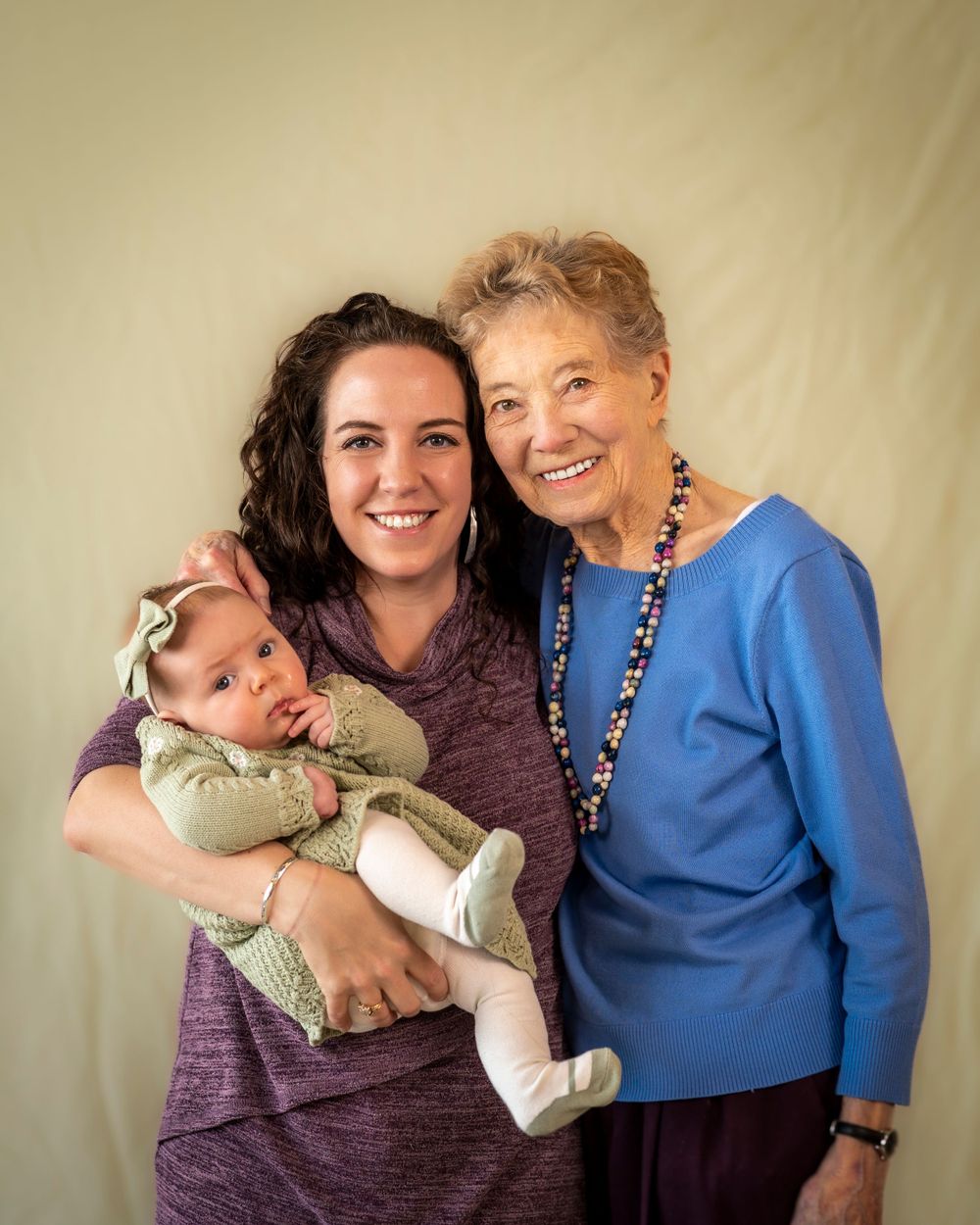 Three generations pose together for a heartwarming portrait against neutral background.