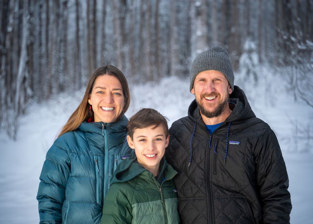 Family of three posing together in a snowy winter forest setting.
