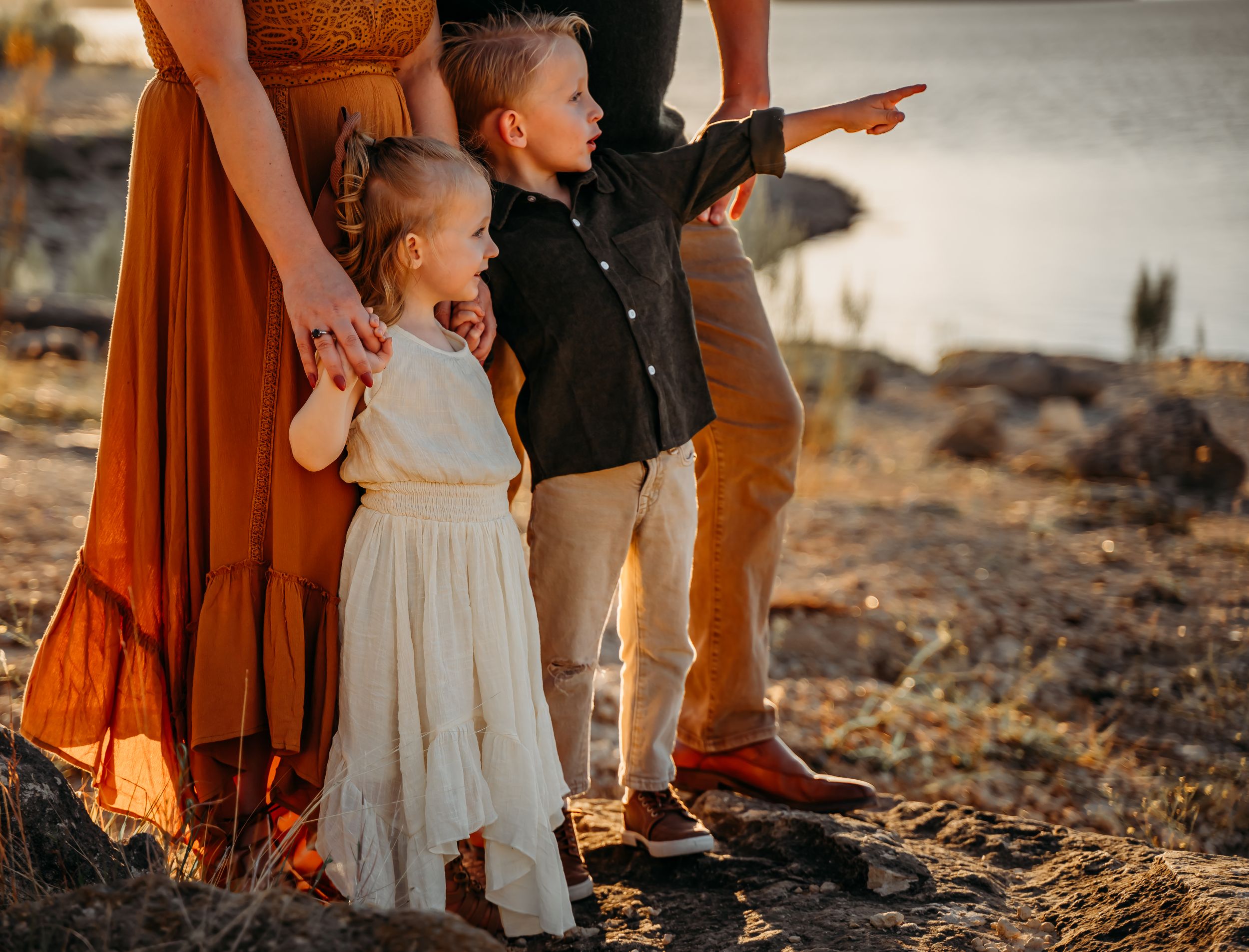 Family in casual attire enjoying sunset view while standing on rocky shoreline.