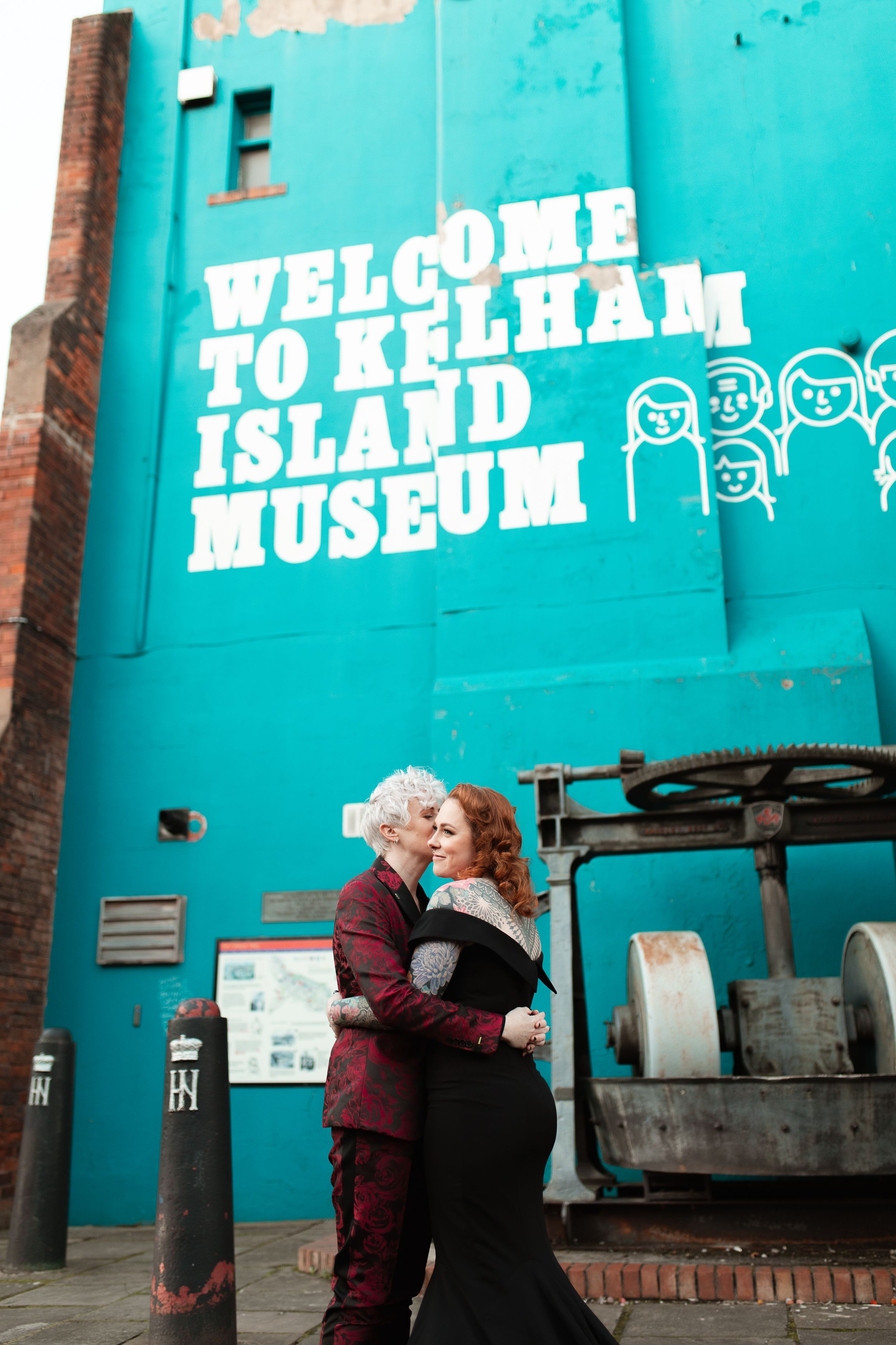 Couple embracing outside turquoise Kelham Island Museum entrance. Sheffield Wedding.