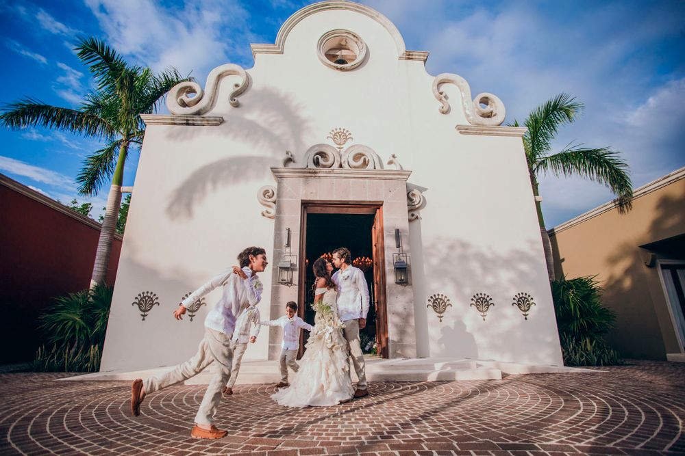 Couple exits ornate white Spanish colonial style church during wedding celebration.