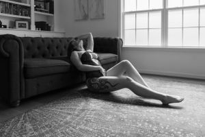Boudoir photography session in black and white. Model wearing black lingerie posing on floor with couch