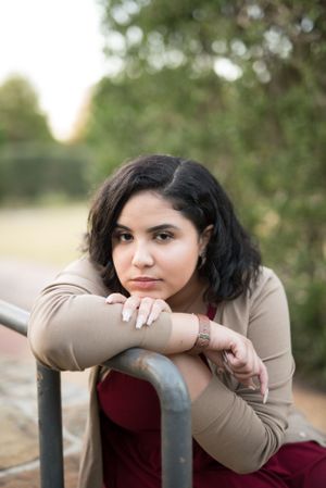 Artistic poses on metal railing with tan cardigan and burgundy dress in outdoor setting.