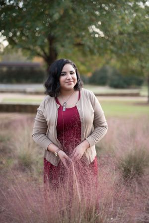 Portrait session in field of pink grass wearing burgundy dress and tan cardigan.