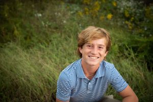 Portrait session in tall grass with sunshine and yellow wildflowers in background.
