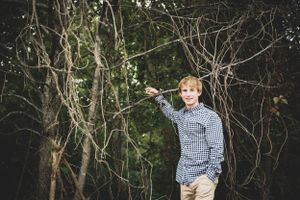 Outdoor casual portrait in checkered shirt against natural foliage backdrop.