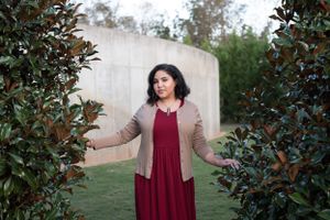 Outdoor portrait session with burgundy dress against greenery and concrete wall.