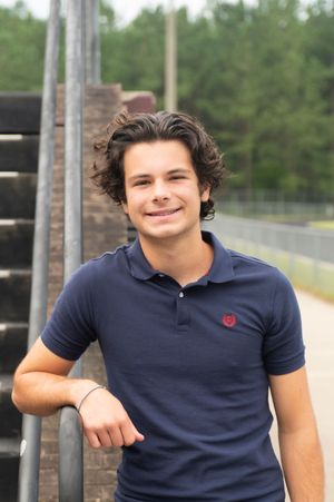 Casual outdoor portrait against brick wall wearing navy polo shirt.