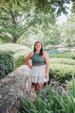 Summer portrait session against a stone wall with garden landscaping.