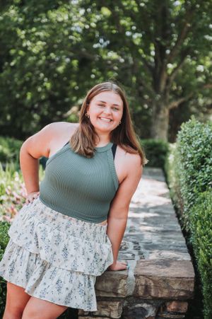 Casual portrait session featuring olive green top and floral skirt against stone wall backdrop.