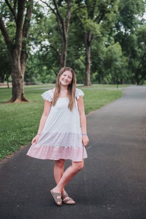 Playful summer photoshoot on a tree-lined path wearing a light pink and white dress.