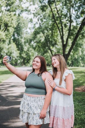 Friends taking selfies and laughing together on a tree-lined walking path.