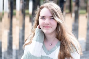 An outdoor portrait featuring a cream and sage striped sweater against a blurred forest backdrop.