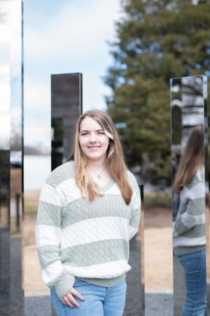 A casual portrait with reflective panels showing a striped knit sweater and relaxed denim.