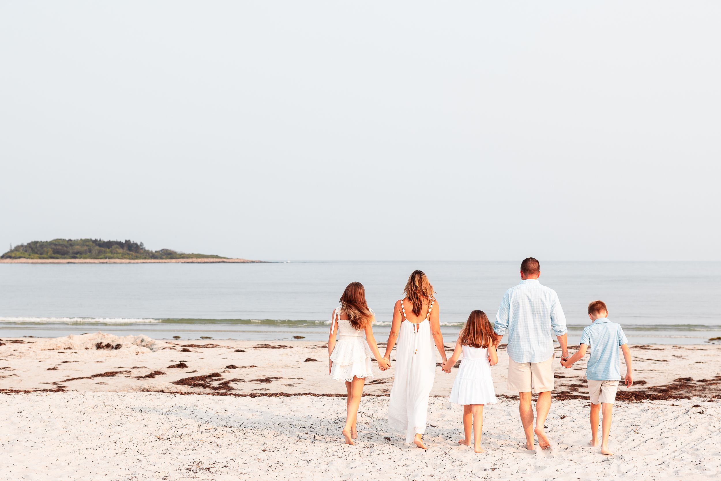 A family of five walk hand in hand towards the water on Goose Rocks Beach in Kennebunkport, Maine