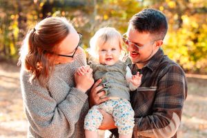 A mother and father play with their toddler girl and make her laugh.
