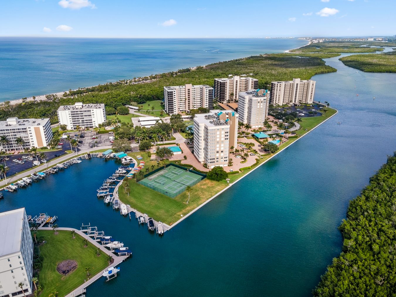 Aerial panoramic view of coastal marina with luxury condominiums and boats docked along turquoise waters in Florida.