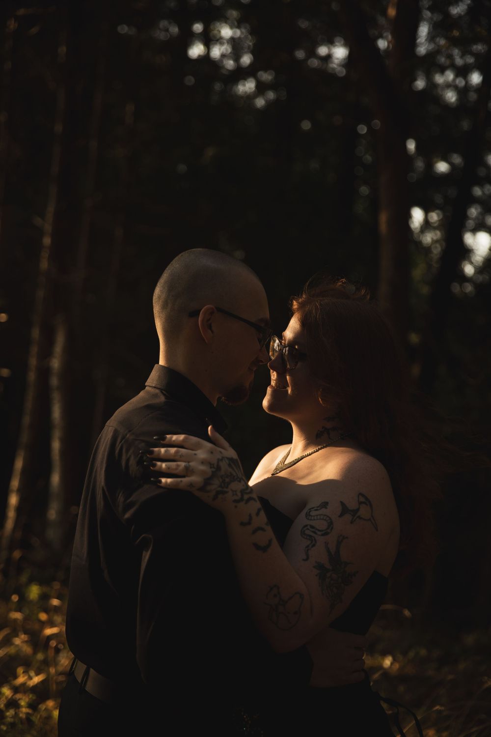 Silhouetted couple embracing in a romantic forest setting during golden hour.
