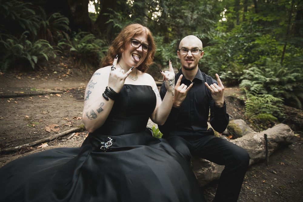 A couple laughs together while sitting on a fallen log in a lush forest setting.