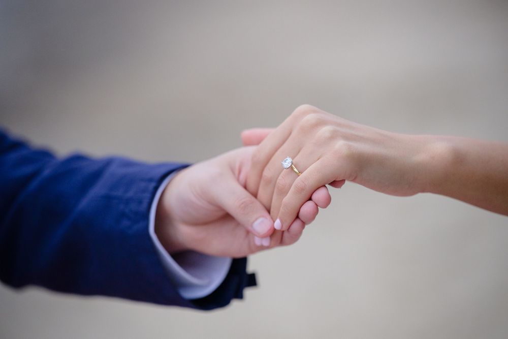 Two hands clasped together with an engagement ring visible on the woman's hand against a blurred background in Cleveland Ohio proposal