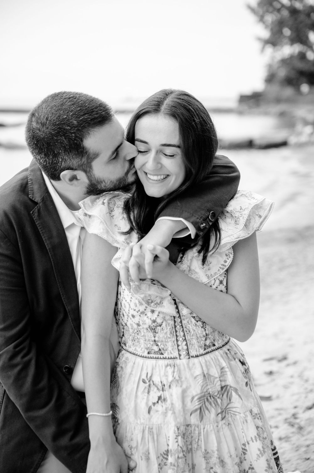 A romantic black and white photo series shows a couple sharing tender kisses on a beach after their engagement in Cleveland Ohio