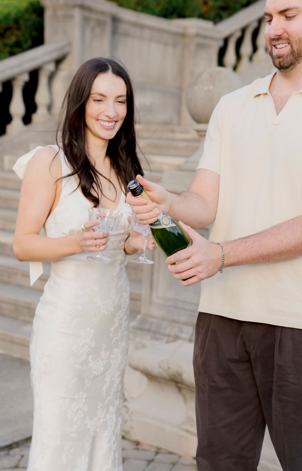 Couple celebrating with champagne on elegant stone steps during wedding photoshoot.