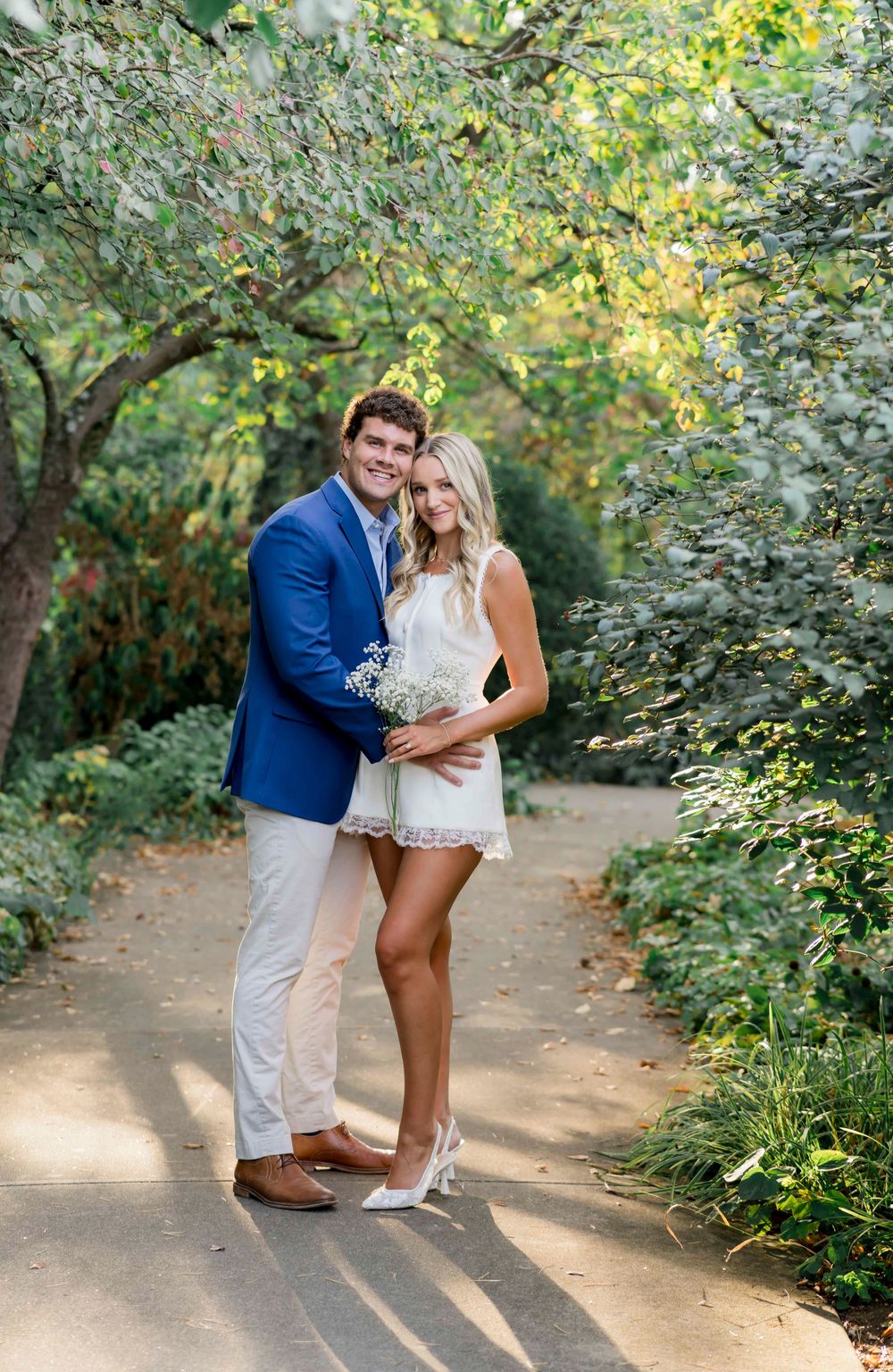 Romantic couple sharing tender moments together on a sunlit nature path surrounded by lush greenery and trees.