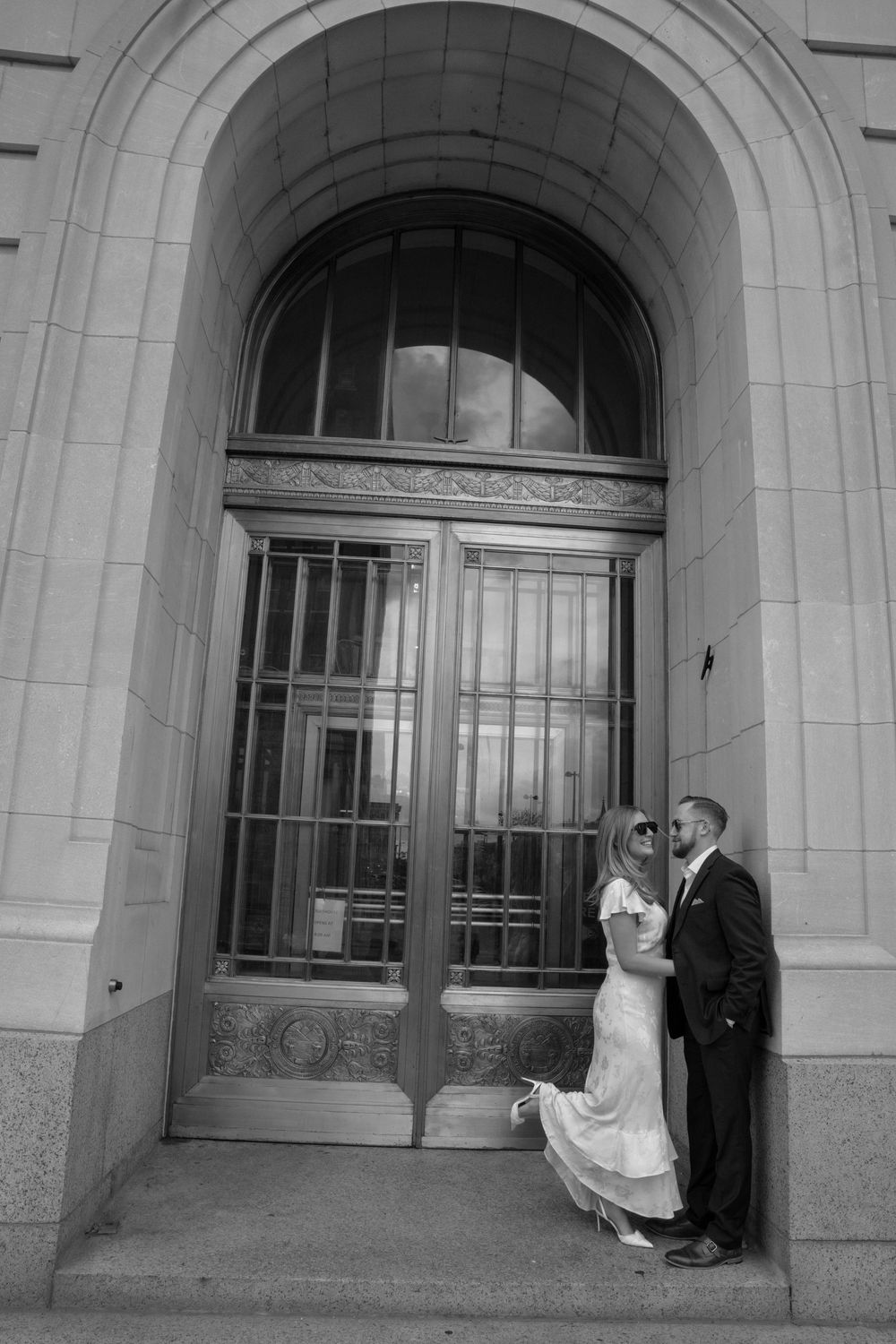 Black and white photo of a bride and groom sharing a romantic moment in an elegant arched doorway.