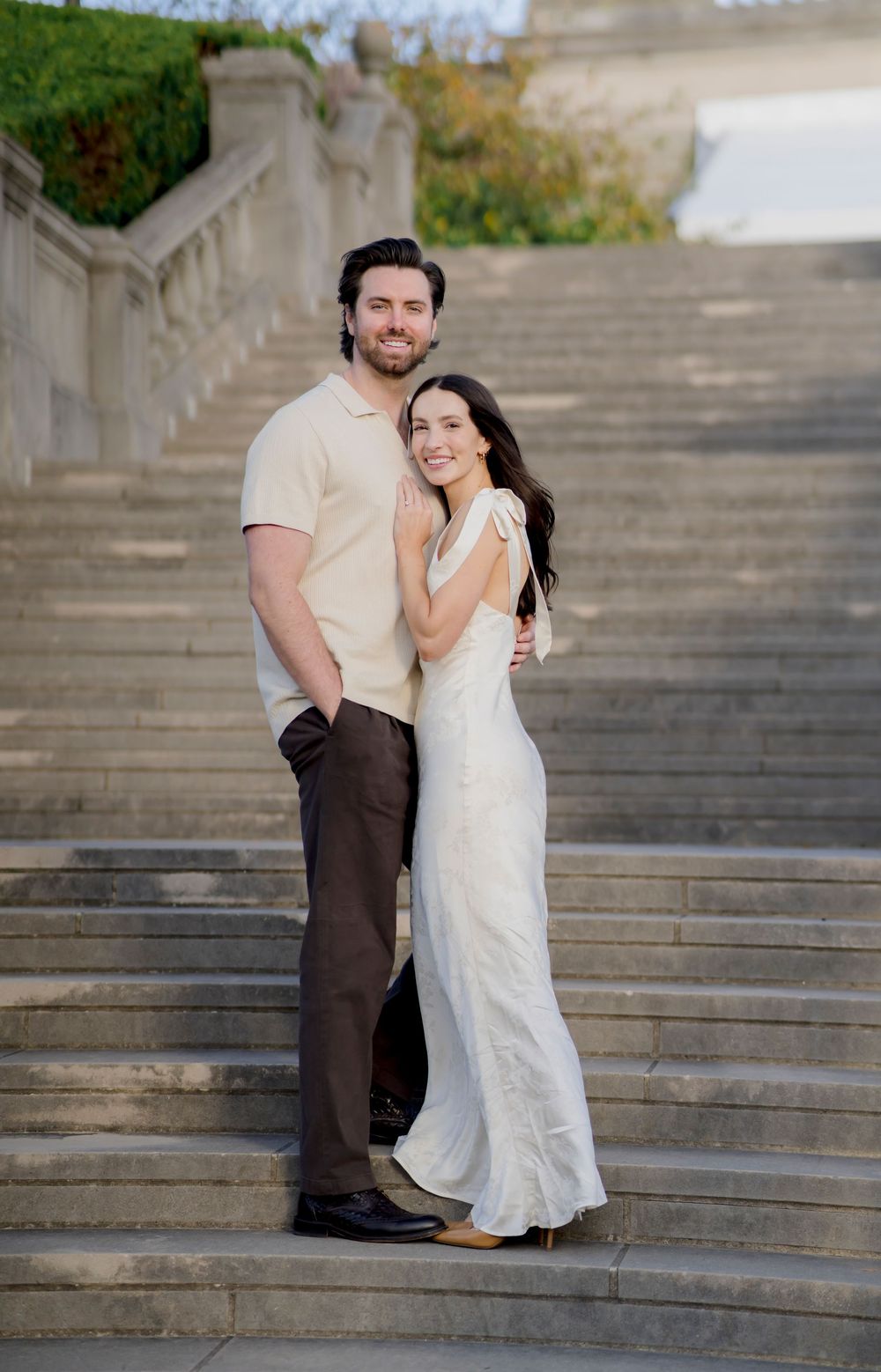 A couple in light colored clothing embraces on stone steps during a romantic photoshoot.