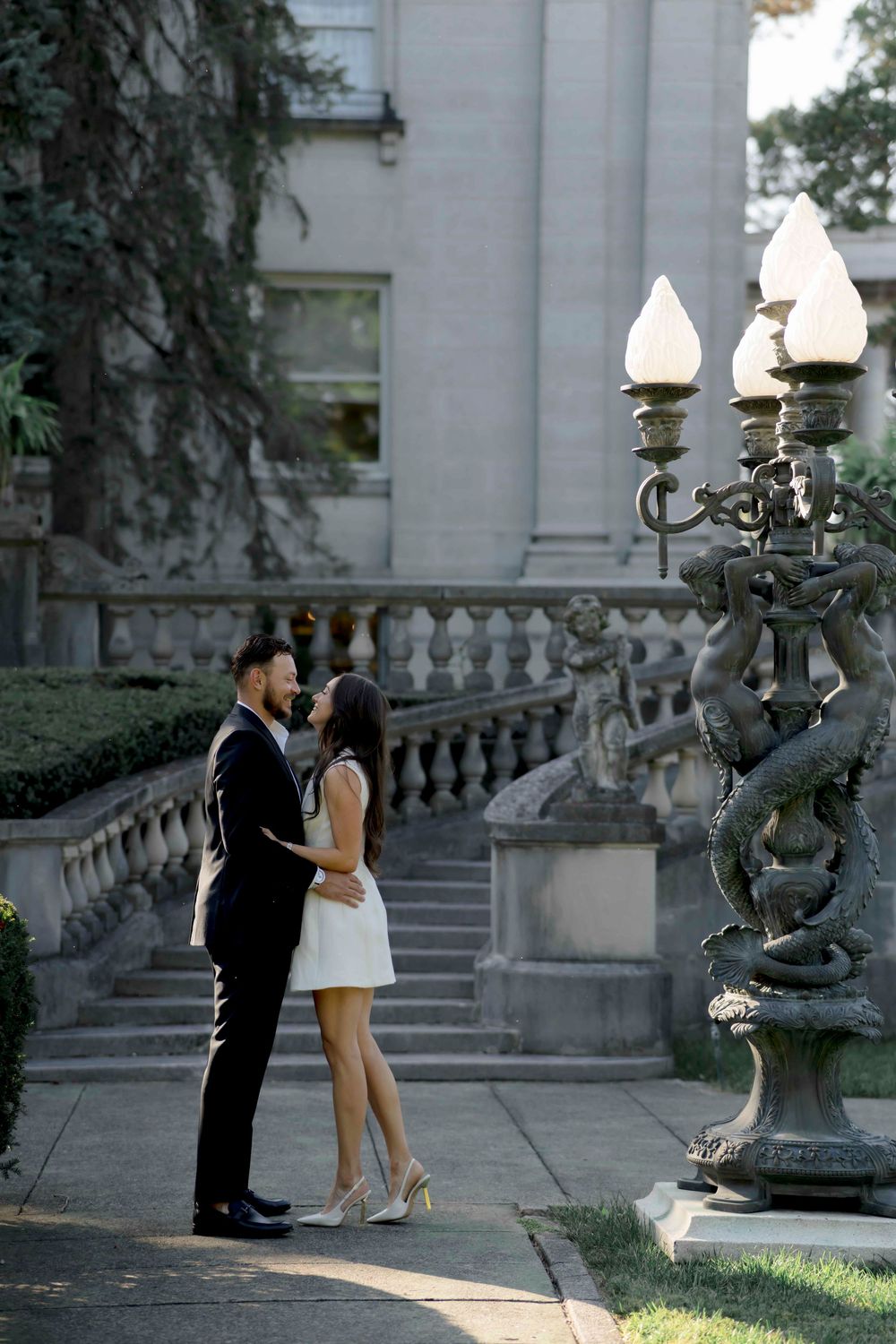 A couple shares an intimate moment on elegant stone steps beside an ornate vintage lamp post at dusk.