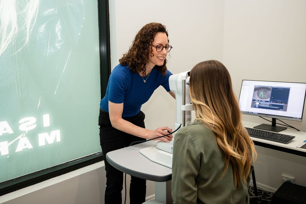 Two people having a discussion in an office setting with a computer monitor and projected display visible in the background.