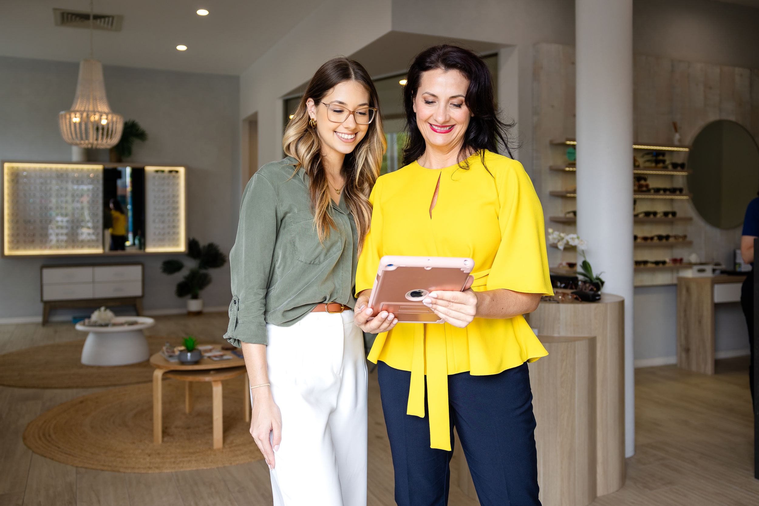 Two people in casual business attire smile while looking at a mobile device in a bright modern office space.