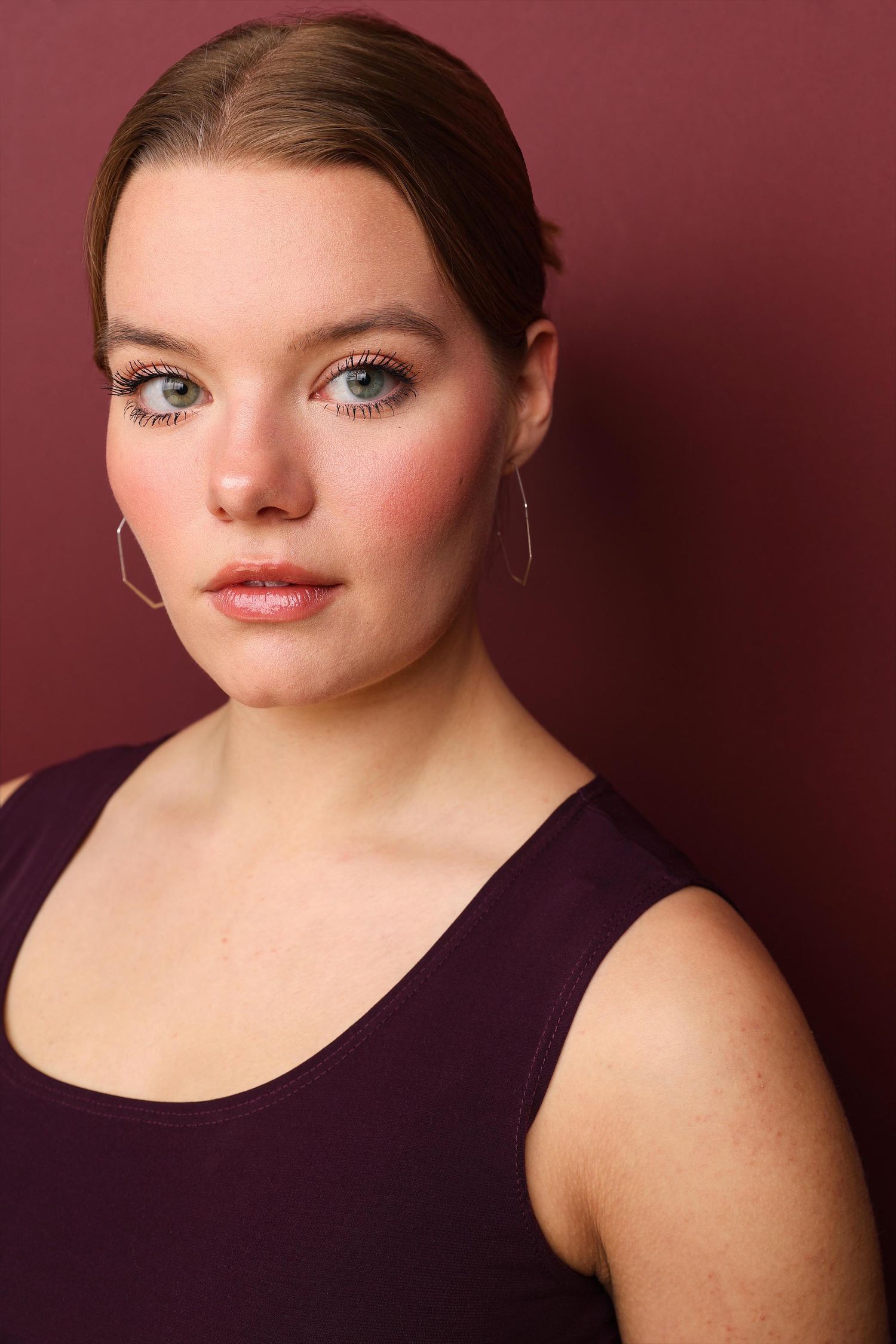 Professional headshot portrait with long dark hair wearing a white top and beige cardigan against a mauve background.