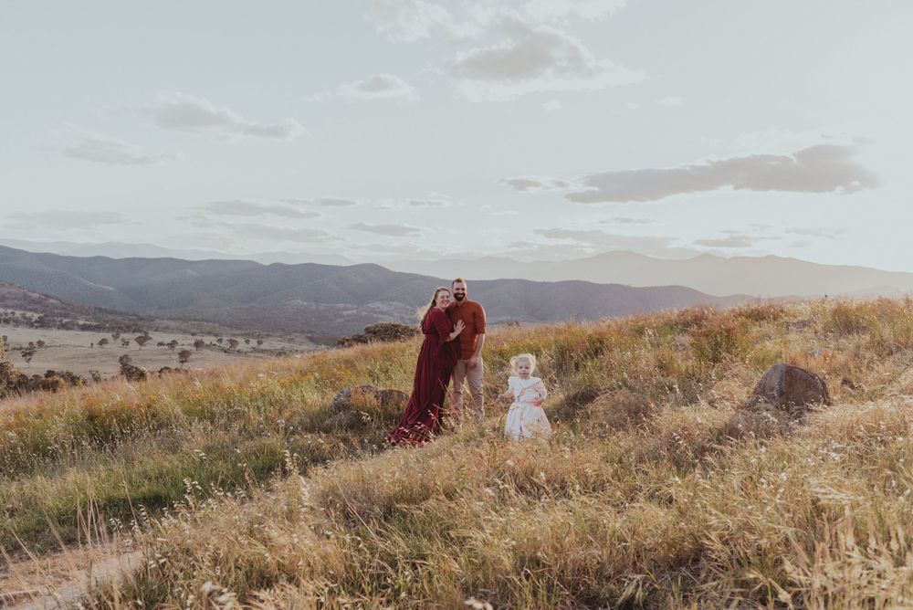 Two figures stand in a flowing dress on a hilltop overlooking a valley at sunset.