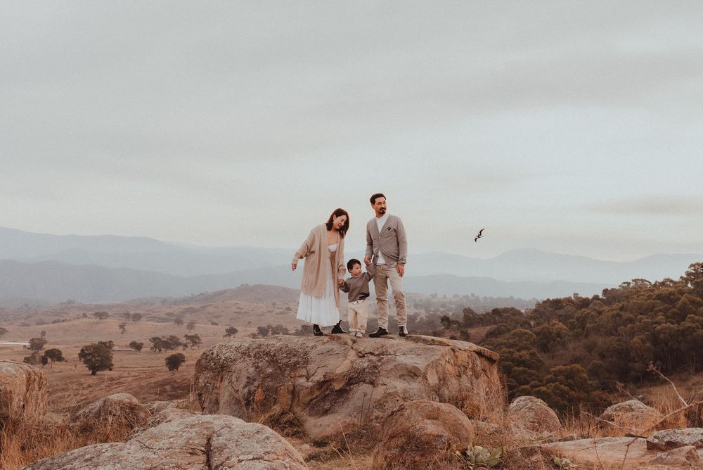 A couple in wedding attire poses together on a rocky mountain overlook at sunset.