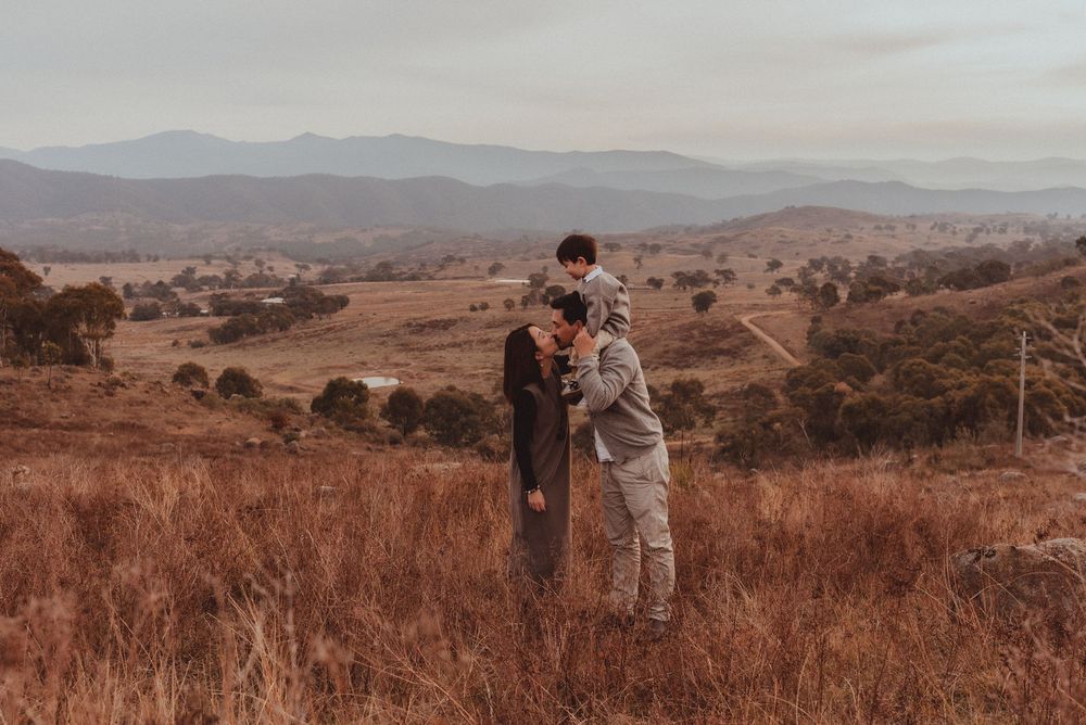Two people embracing in a scenic mountain landscape during golden hour with dry grass and rolling hills in the background.