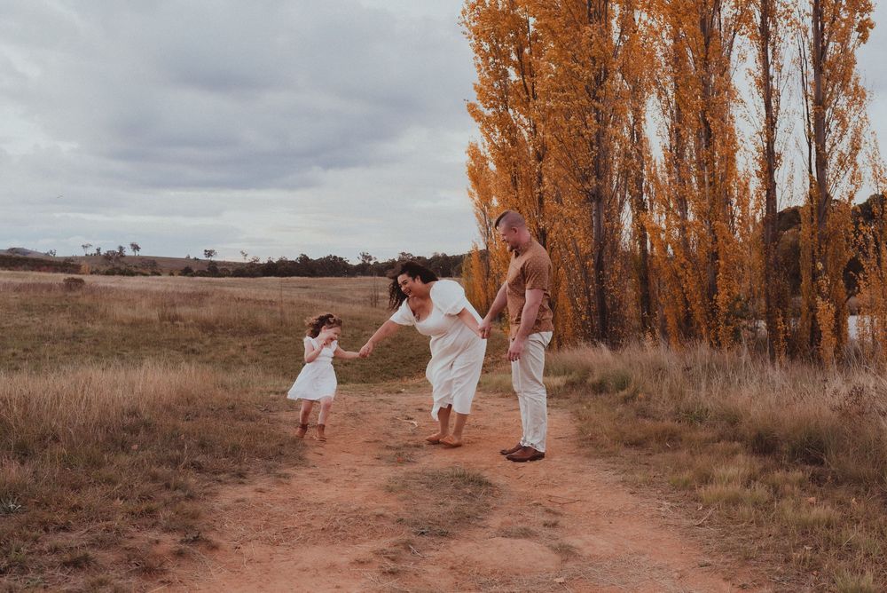 People in white outfits walking together along a dirt path lined with autumn trees at sunset.