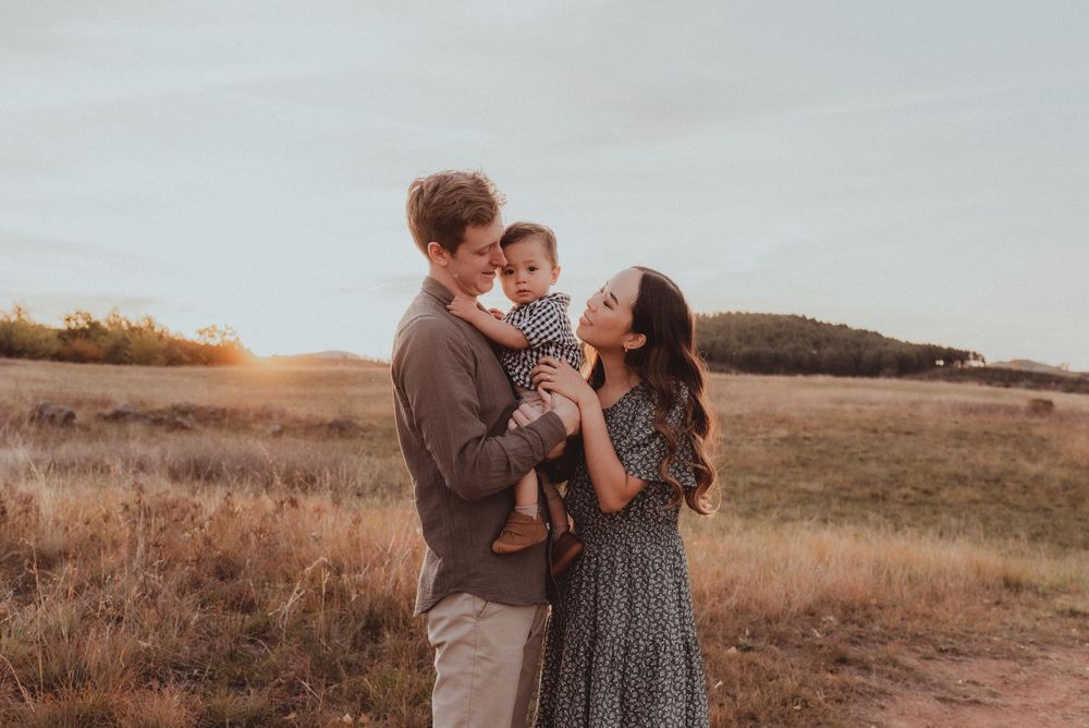 A family shares a tender moment together in a golden field at sunset, surrounded by autumn grasses and rolling hills.