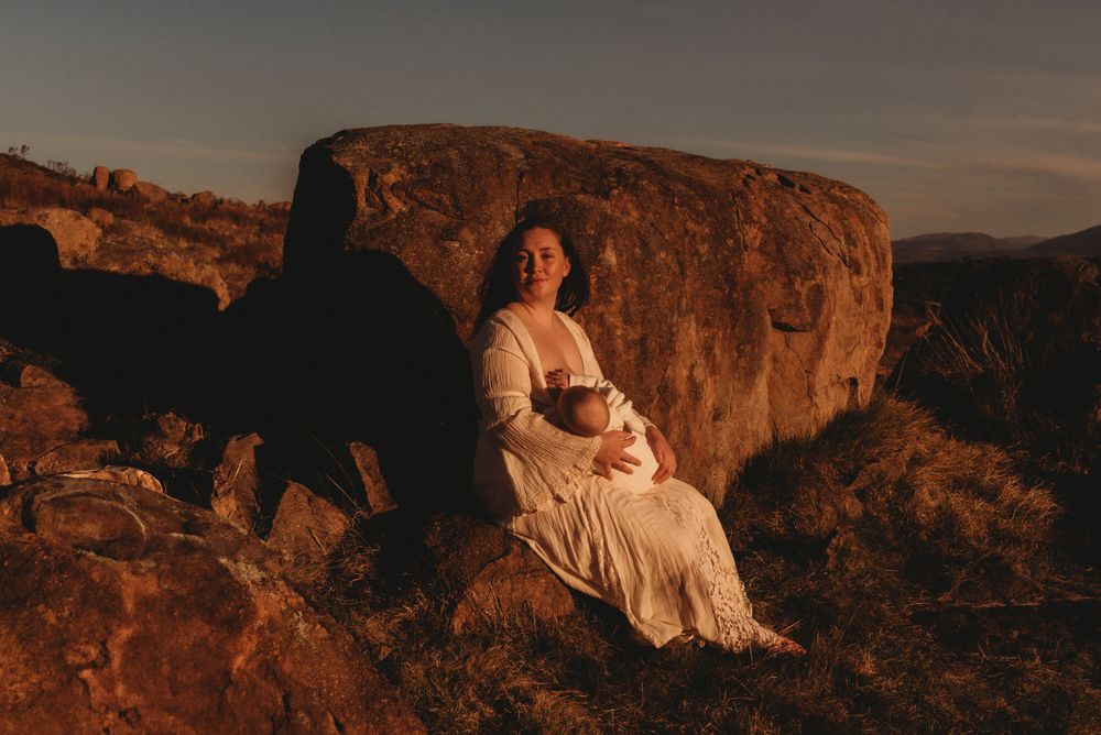 A person in white sits with a child against dramatic rock formations at sunset.