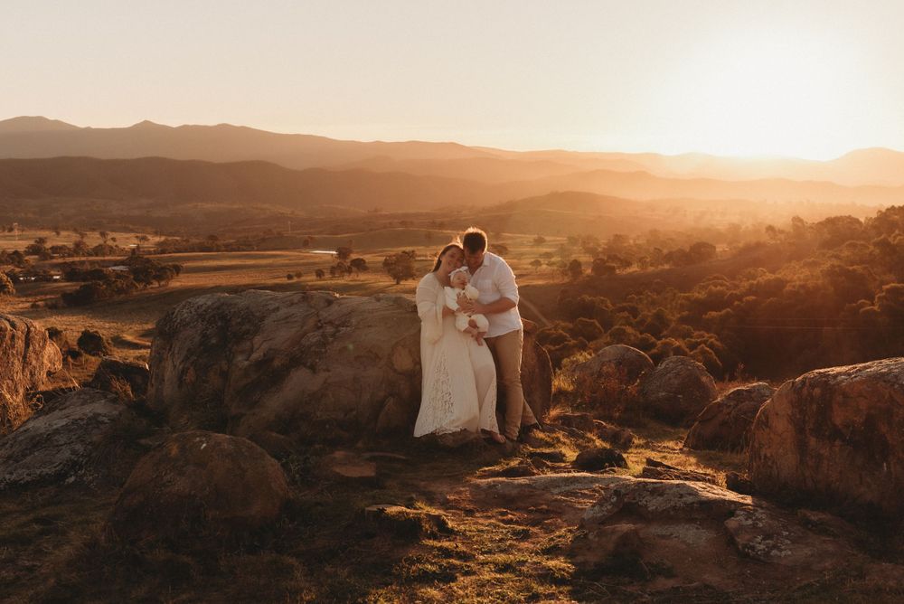 A romantic couple stands on rocky cliffs at sunset in a mountainous landscape.