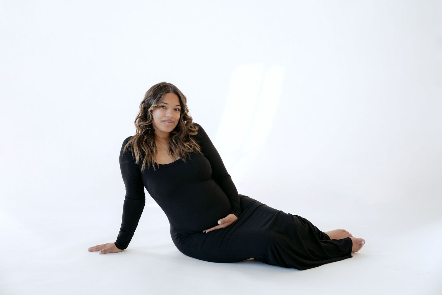 Mama-to-be wearing a tight black dress to accentuate baby bump during in studio maternity portraits in stillwater MN with Jagger Rose Photo