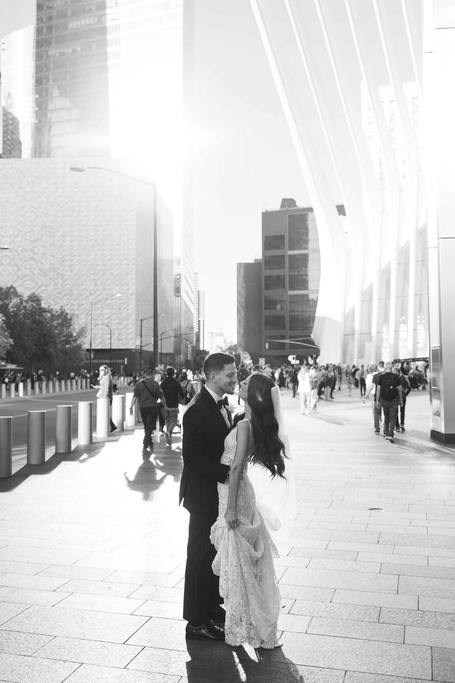 Black and white photo of newlyweds facing each other on sunny city street with skyscrapers in background.
