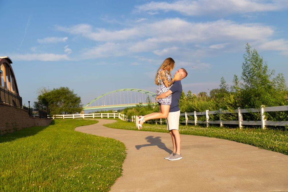 Engagement Session with a male picking up the female and the Veteran's Memorial Bridge in the background.