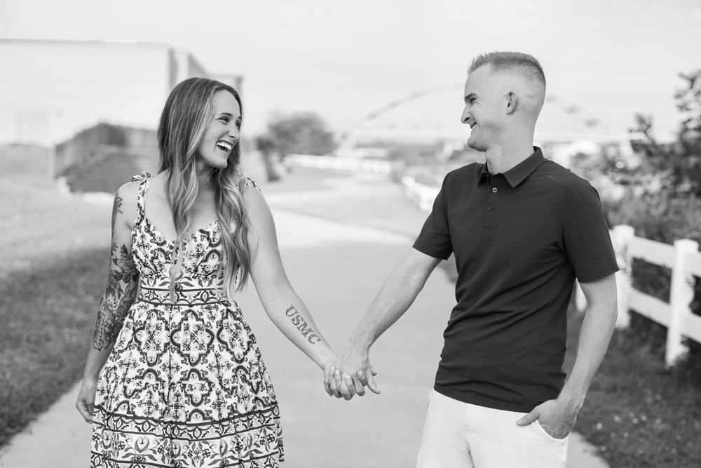 Black and white candid engagement photo of a couple laughing taken in Sioux City with the Veteran's Memorial Bridge in the background.