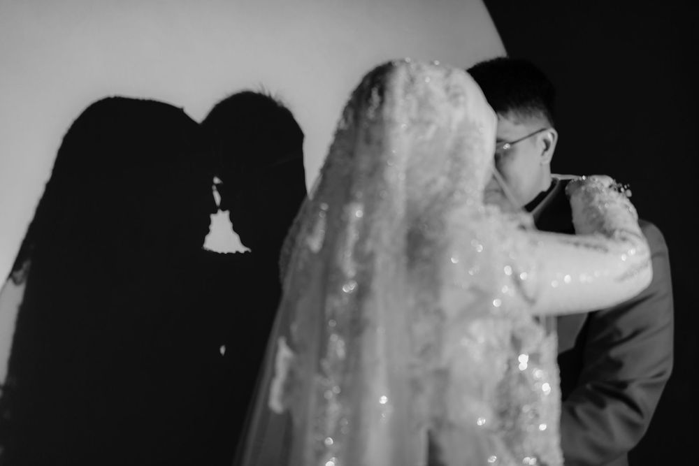 Black and white wedding photo of bride and groom kissing with romantic shadow silhouette on wall.