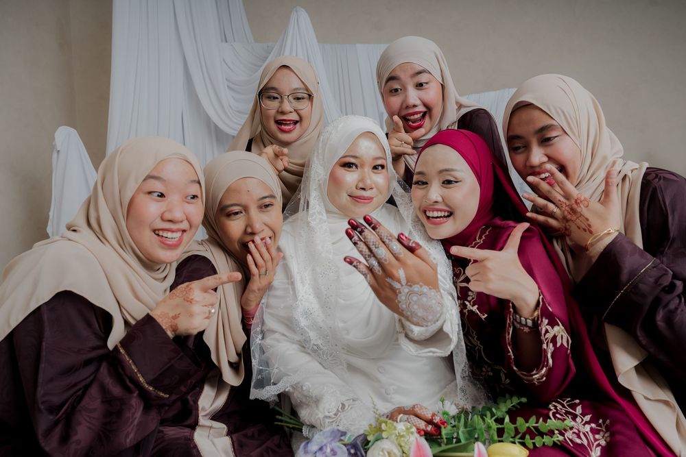 A joyful bride in white hijab poses with seven friends in colorful hijabs, showing rings and smiling together.