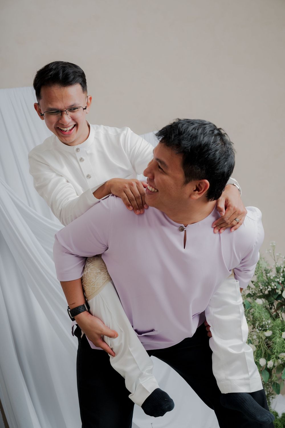 Two men in traditional Malay baju kurung laughing together at a formal event, sharing a joyful moment.