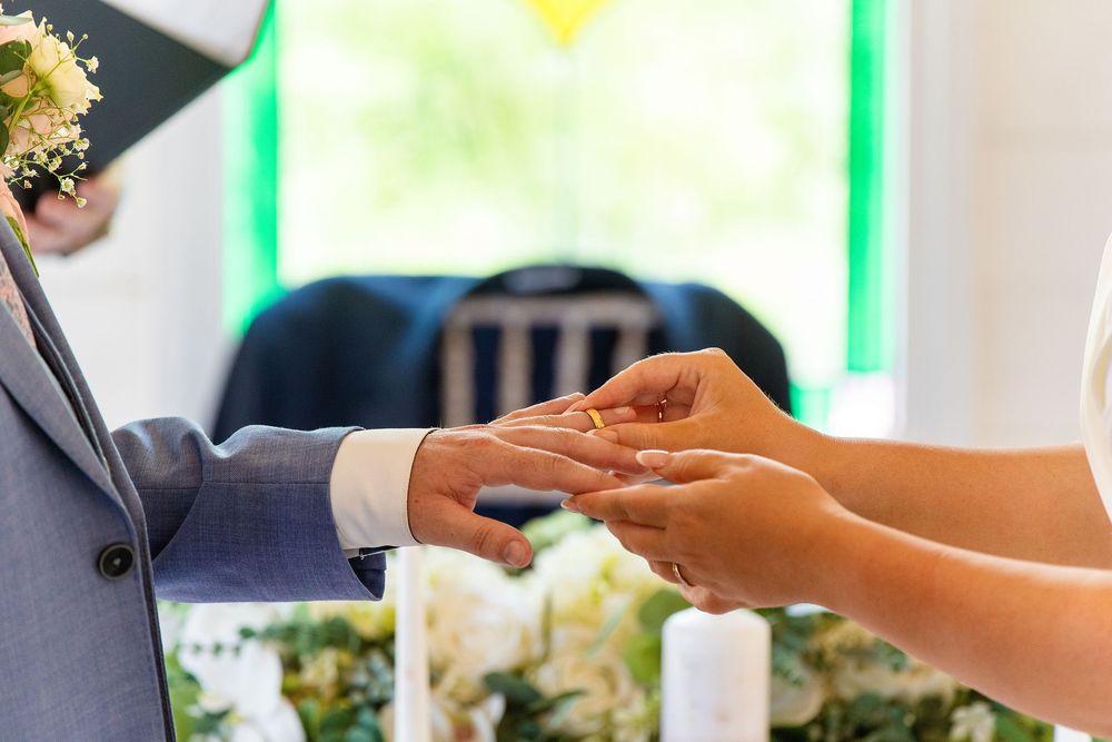 Close-up of bride placing gold wedding ring on grooms hand during ceremony.