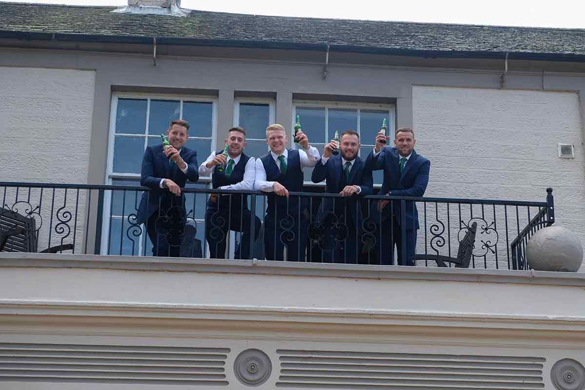 Group of men in suits posing on the balcony at historic Blaithwaite House wedding venue near Wigton