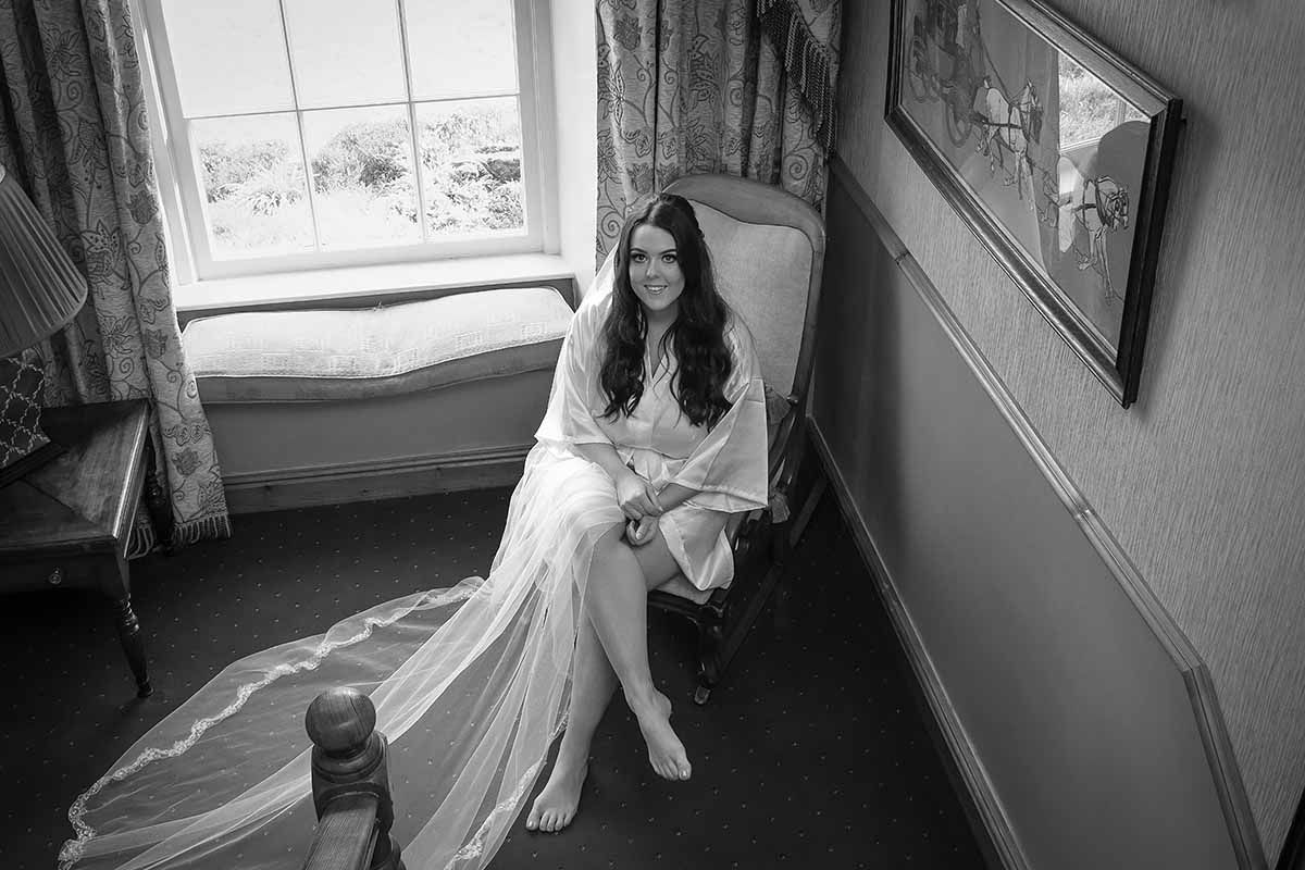Black and white photo of a bride in a white gown sitting by a window at New House Farm wedding venue Lorton Cockermouth